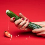 person holding green cucumber on red table